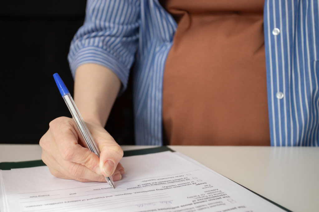 Pregnant woman signing an insurance form for maternity coverage, prenatal care, and childbirth expenses