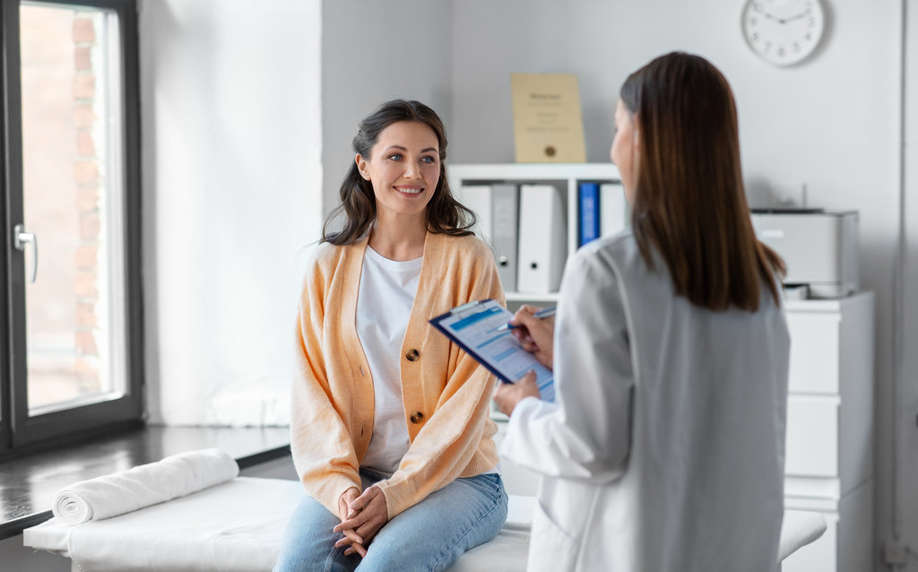 medicine, healthcare and people concept - female doctor with clipboard talking to smiling woman patient at hospital