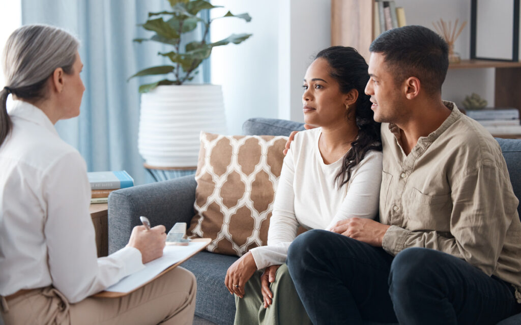 Couple on sofa, therapist and counselling for support, love and help with relationship advice together. Man, woman and psychologist in conversation, healthy communication and healing marriage therapy